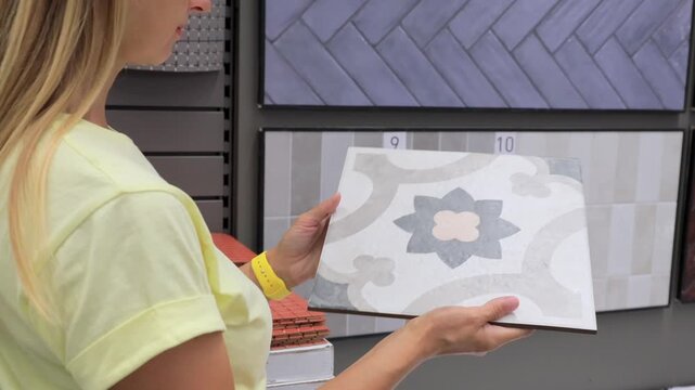 Woman choosing decorative ceramic tile with floral pattern in hardware store