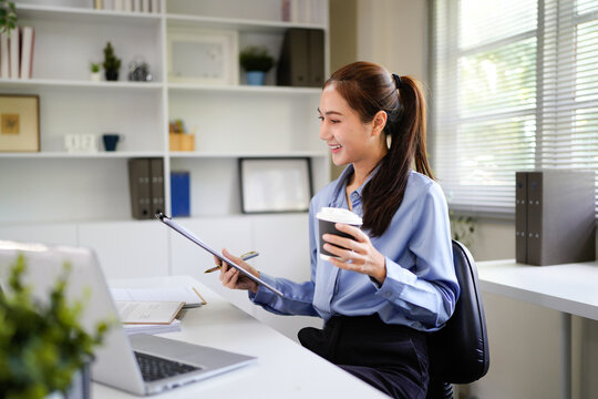 Focused female executive analyzing financial reports while holding coffee cup at office desk.