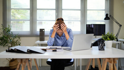 Asian businesswoman suffering from headache and touching her head while using laptop computer at...
