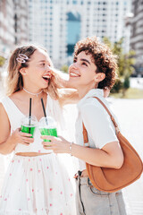 Two young beautiful smiling hipster female in trendy summer clothes. Carefree women posing outdoors. Positive models holding and drinking fresh cocktail smoothie drink in plastic cup