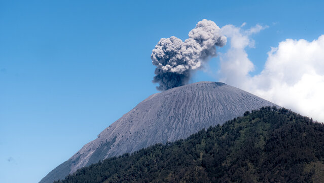 Volcanic eruption of Mount Semeru in Indonesia, captured from a nearby area showing dramatic ash plume and mountain slopes - Powered by Adobe