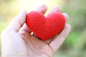 A person's hand holding a handmade red heart made from crochet fabric