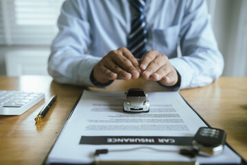 Fototapeta premium Businessman protects his car by placing his hand on the insurance contract, which symbolizes safety, security, trust and vehicle protection agreement.