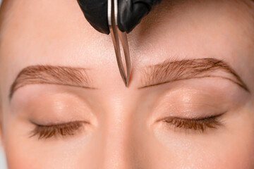 Eyebrow shaping session in a beauty salon with a focused aesthetician preparing to trim brow hairs...
