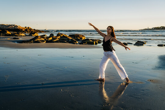 Young woman practicing ballet poses on the beach at sunset