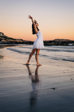 Young woman dancing barefoot on the beach at sunset