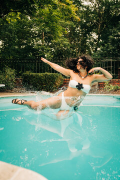 Woman jumping into swimming pool wearing white bikini and sunglasses