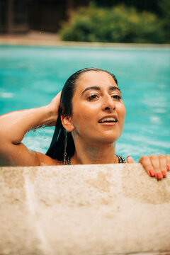 Beautiful woman relaxing in swimming pool, holding wet hair