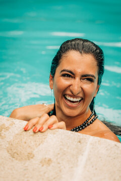 Happy woman laughing in swimming pool holding edge