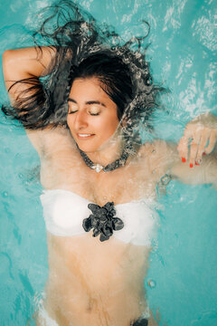 Young woman relaxing floating in a clear blue swimming pool