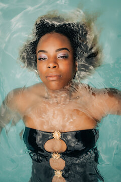Young black woman floating in turquoise water wearing elegant swimsuit