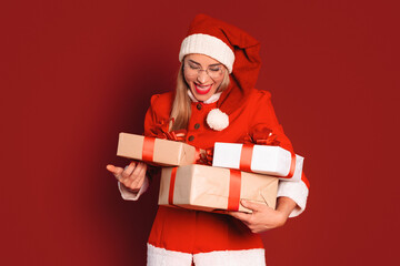 Woman in red Christmas outfit joyfully holds wrapped gifts against a festive red background