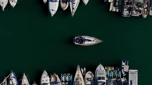 Aerial view of a boat sailing through a dark green marina surrounded by docked boats and Yachts