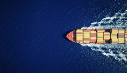 High aerial overhead view of a large industrial container cargo vessel sailing over the ocean with copy space