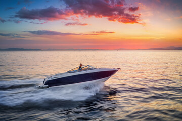 A motorboat sails ove the calm ocean with high speed during sunset time