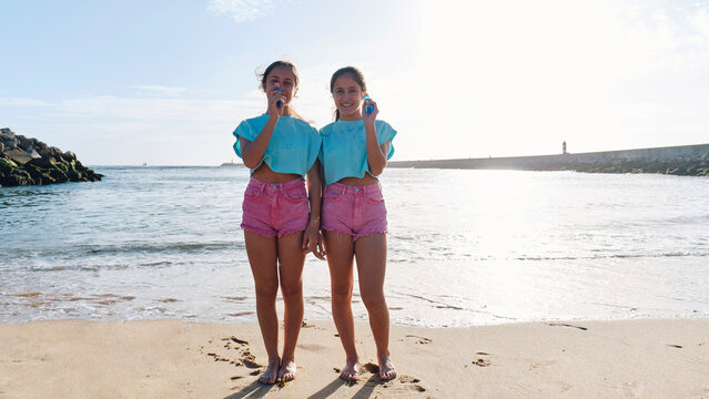 Twin sisters in matching outfits holding squirt guns at beach