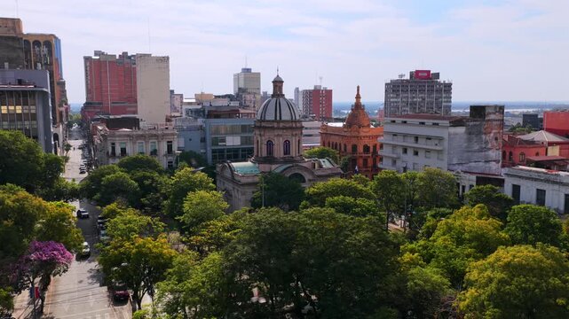 Drone video capturing sweeping views of Asuncion's Pantheon of Heroes. The lush greenery contrasts with historic and modern architecture under bright daylight.