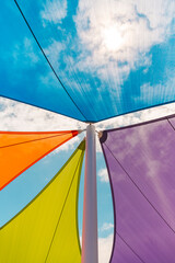 Colorful shade sails stretched above pole viewed from below, vibrant fabric triangles in blue, orange, green, and purple against bright sky