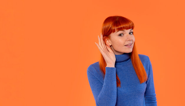 Woman with red hair listening attentively while wearing a blue turtleneck against an orange background, highlighting an engaging and casual atmosphere