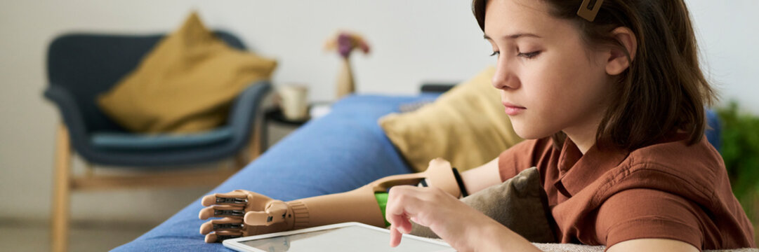 Girl with prosthetic arm using digital tablet on sofa indoors