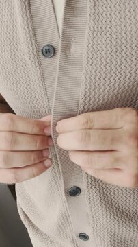 Vertical closeup of bearded man buttoning knitted shirt and adjusting collar while preparing to head out, focusing on grooming and dressing