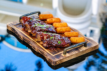 Tantalizing BBQ ribs, glazed with succulent sauce and sesame, served alongside potato croquettes on an elegant serving tray, showcasing ideal cuisine presentation for culinary appreciation.