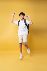 Joyful student jumping with backpack celebrating a successful school day isolated on yellow