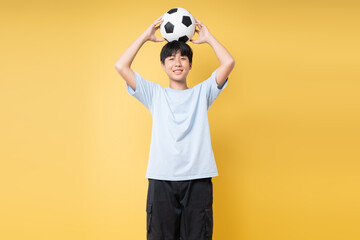 Teenager smiles while balancing a soccer ball on his head against a bright yellow background