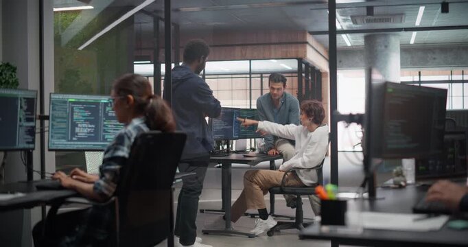 Creative Team of Diverse Specialists Having a Conversation at a Workplace Next to Computer. Two Male Software Engineers and a Female Developer Discussing a Software Code for Their Digital Project