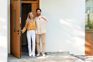 Happy couple showing keys of new home standing at the door