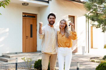 Happy couple celebrating buying new house showing keys in front of home