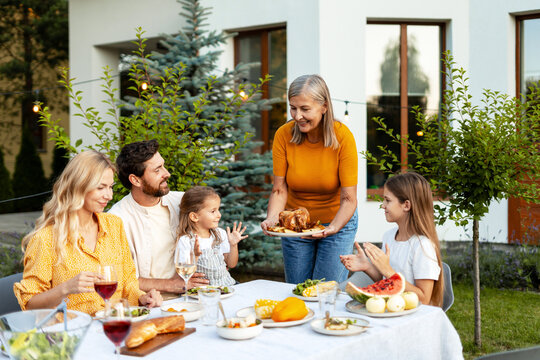 Grandmother serving roasted turkey to family at garden party, festive table