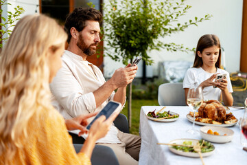 Family using smartphones at dinner table outdoors, text message, reading news, playing games