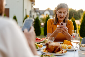 Senior woman using smartphone while having dinner with family in garden
