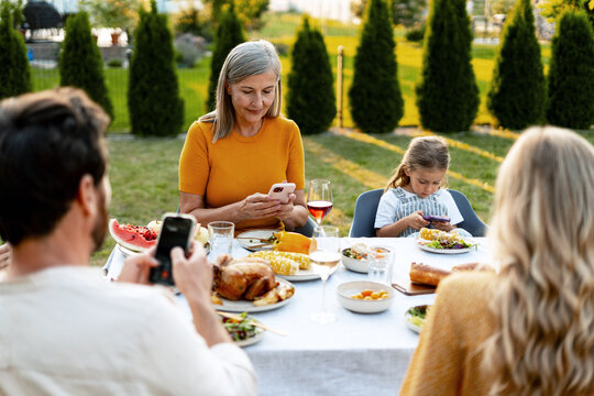 Family using smartphones while having dinner together outdoors, thanksgiving day - Powered by Adobe