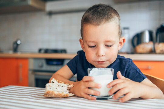 Child enjoying bread and drinking milk in kitchen at table