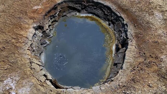 Top view of a slightly bubbling mud volcano. A tourist destination in Gobustan, Azerbaijan. The volcano is surrounded by a desert landscape where no vegetation is visible.