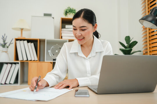 happy woman writing cocument or paperwork with laptop at home office