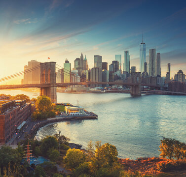 Panoramic view of the Brooklyn Bridge and Manhattan skyline at golden hour with warm sunlight and dramatic evening sky over the East River.