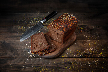 Black whole grain bread loaf on rustic brown wooden background. Traditional and hearty baked food.