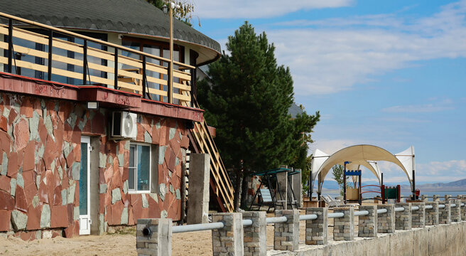 Stone house with terrace and gazebo at Bukhtarma Reservoir resort in early autumn. Pine trees and lake shore create a cozy and relaxing atmosphere for vacation and leisure