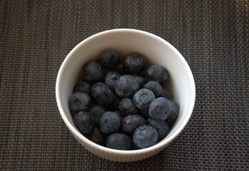 Fresh ripe blueberries in a white ceramic bowl with gray background, close-up shot with copy space for text.