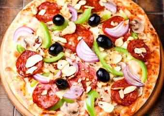 Pizza with chorizo ​​sausage, mozzarella cheese, green pepper and black olives. Rustic wooden background. Soft focus.	