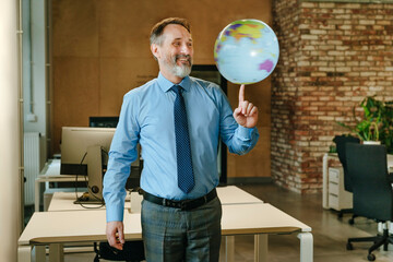 Businessman spinning globe on finger in modern office smiling