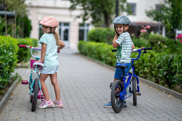 Two confident youngsters enjoy a bike ride in the city, showcasing their friendship and joy. The image highlights health and the importance of safety measures like wearing helmets. 