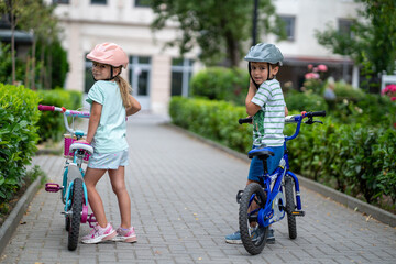 Two confident youngsters enjoy a bike ride in the city, showcasing their friendship and joy. The image highlights health and the importance of safety measures like wearing helmets. 