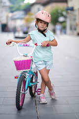 Cute girl wearing cycling helmet and riding bike at park. Portrait of a playful funny girl in a pink safety helmet on her bike