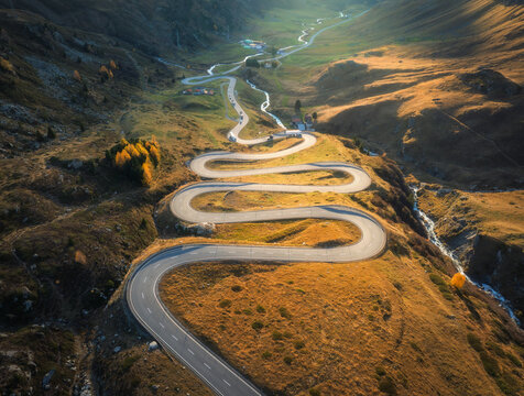 Aerial view of winding mountain road, river in alpine valley at sunrise in autumn. Top drone view of road in Swiss mountain pass, yellow grass, trees in fall. Colorful landscape. Alps in Switzerland - Powered by Adobe