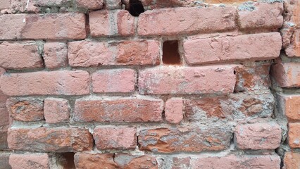 Antique brickwork. Fragment of facade of dilapidated building. Close-up of red brick wall. Holes and voids from broken stones. Texture of old brick. Abstract background