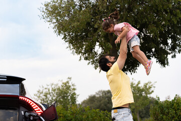 Father lifting his daughter in the air while charging electric car during road trip